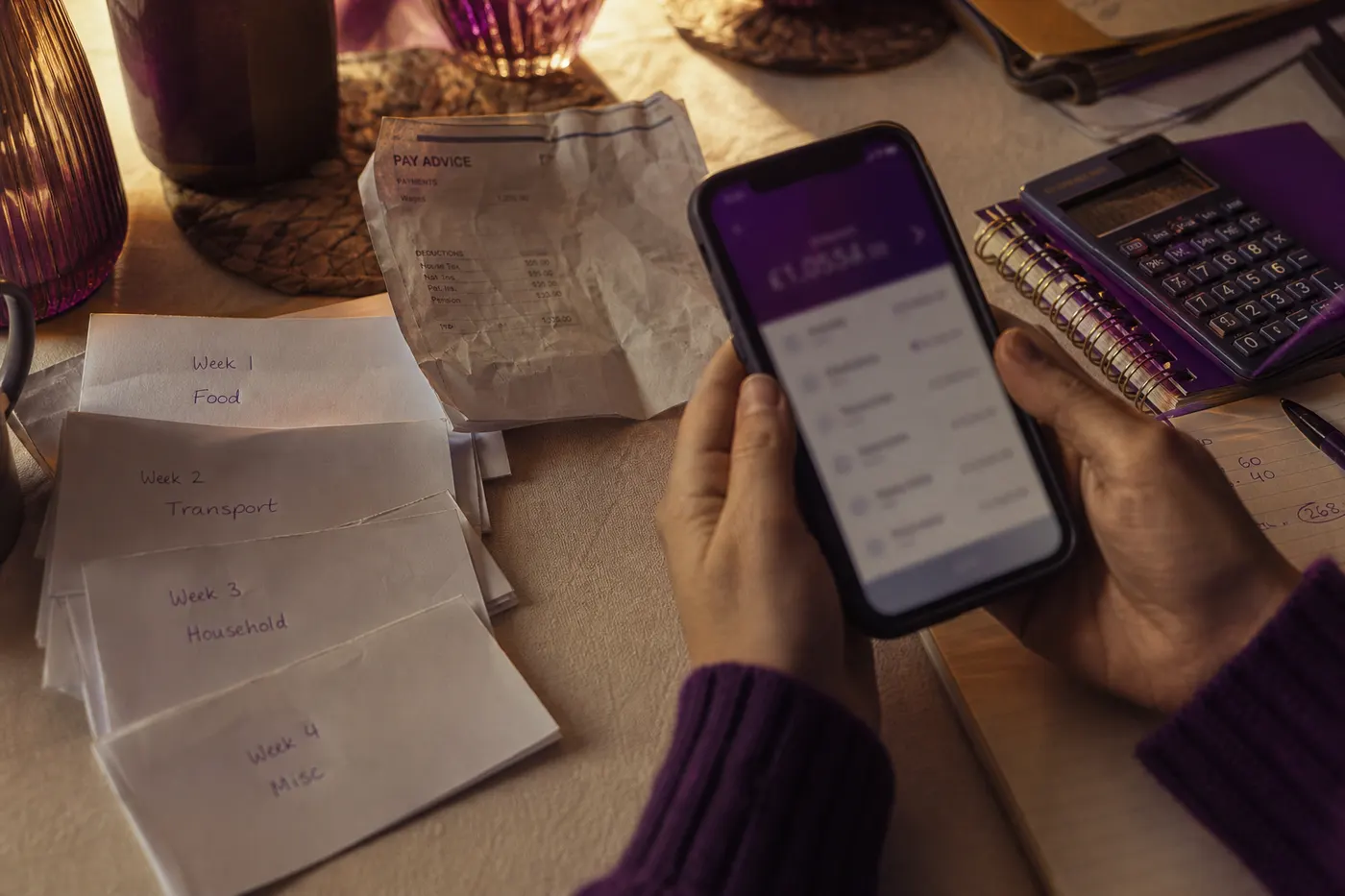 Hands checking several banking apps over weekly pay slips and a calculator